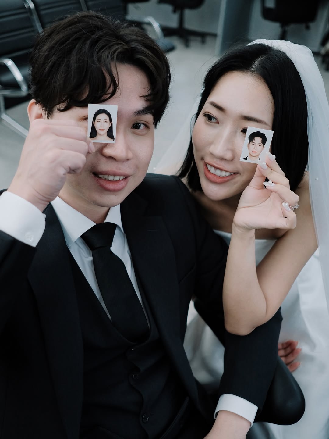 The couple laughing, each holding up a small ID photo of the other